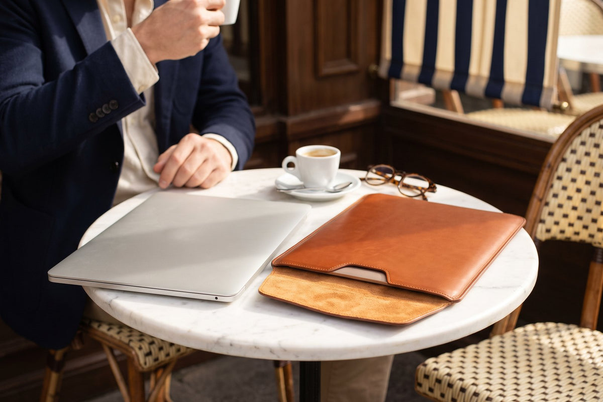 Ordinateur portable fermé à côté d'une housse en cuir cognac sur une table de café en marbre