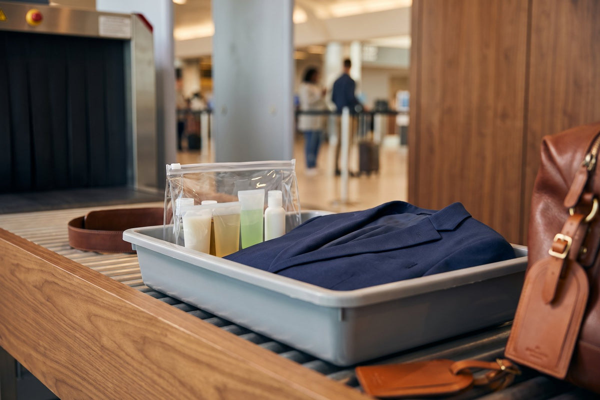 Bac de contrôle de sécurité avec un sachet transparent de petits flacons et une veste marine, à l'aéroport